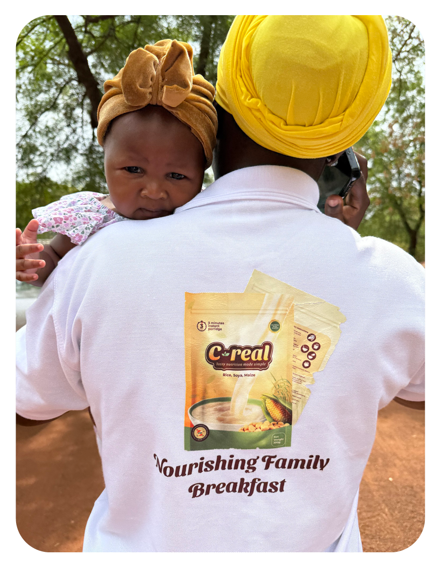 A lady holds a baby over her shoulder and has the C-Real branding on the back of her t-shirt.
