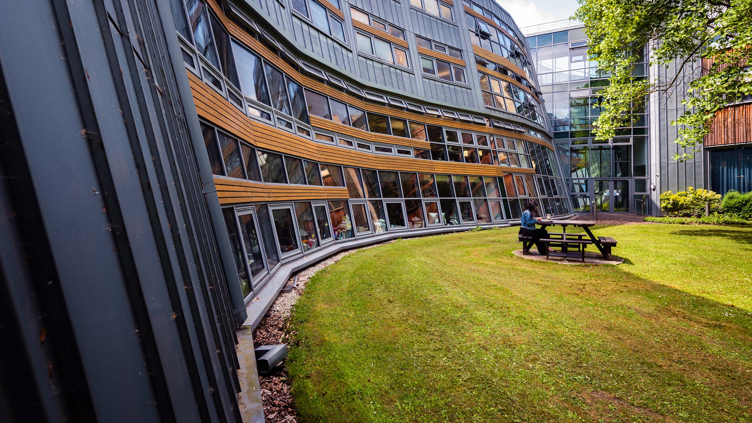 Student sitting at a picnic table in green space outside the Berrick Saul Building.