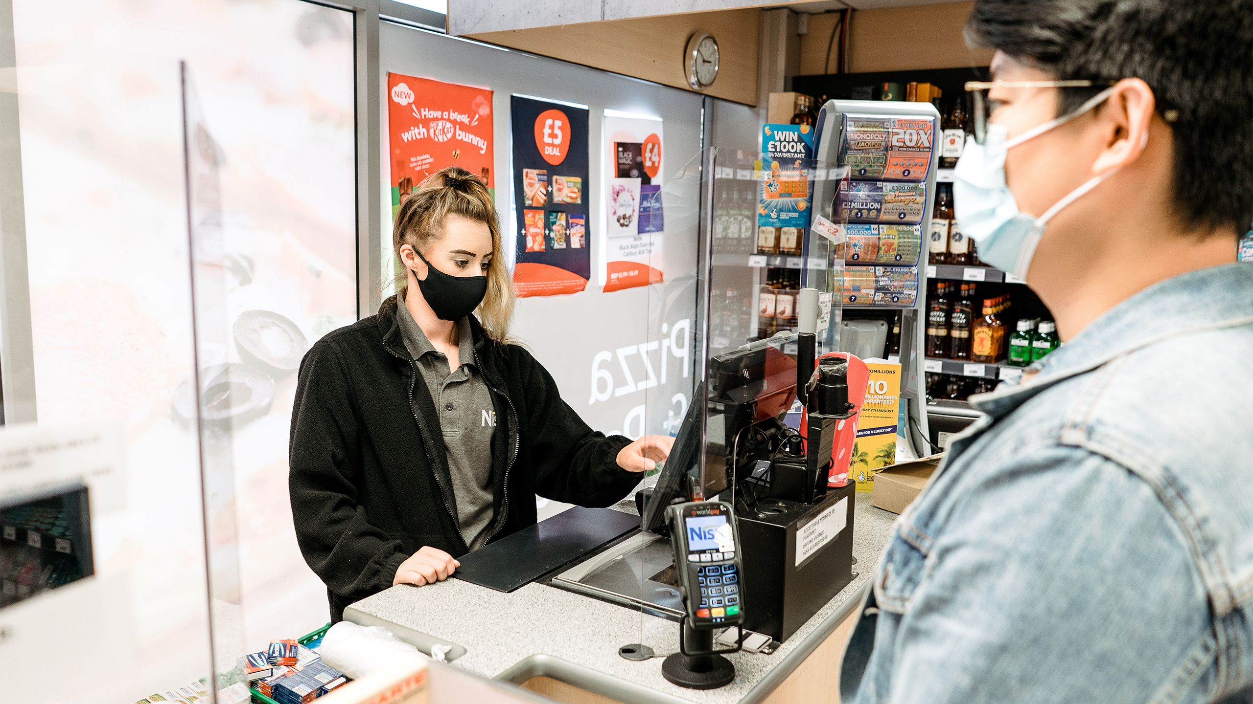 Staff member in the Nisa store serving at the till wearing a face covering