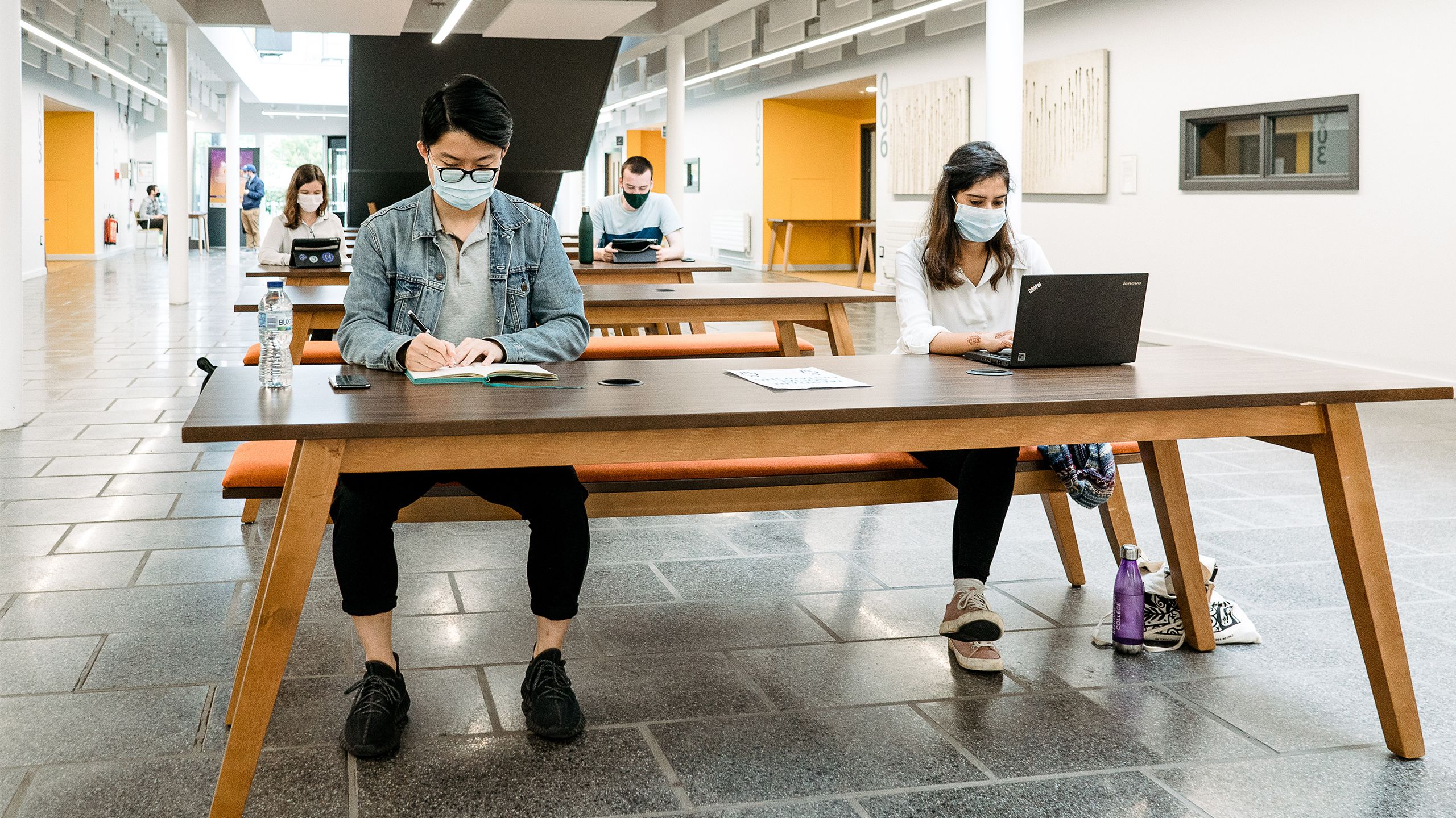 A group of students wearing face coverings and socially distancing while they study