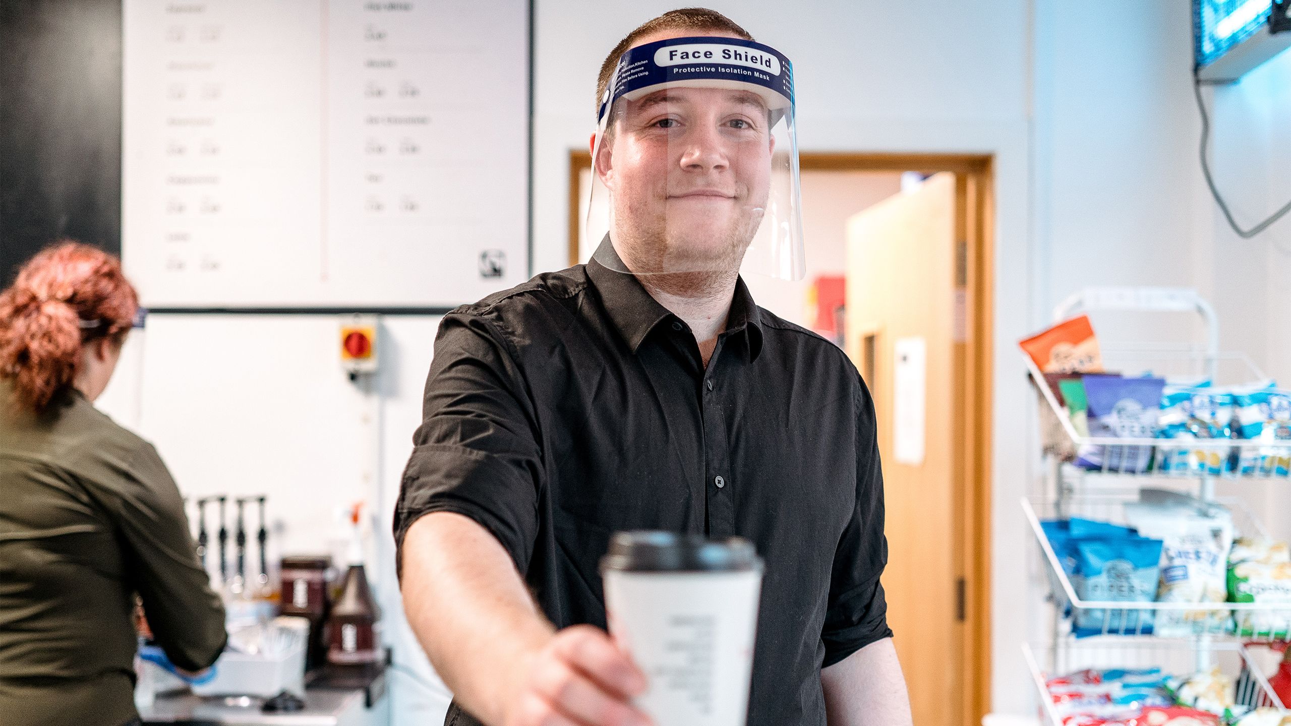 Staff member in the coffee shot wearing a face shield serving coffee