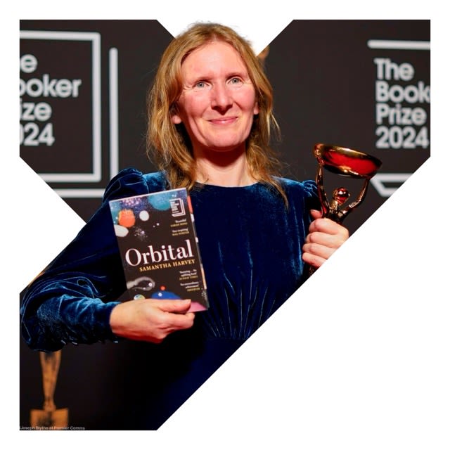 Samantha Harvey is smiling, holding a copy of her book 'Orbital' and an award in her other hand